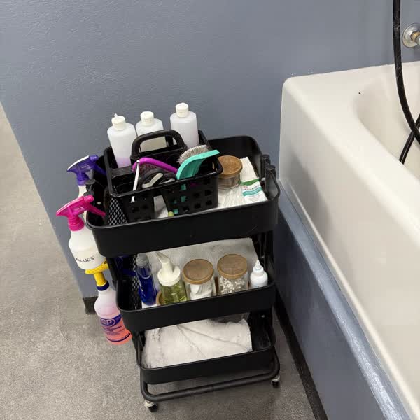 A supply cart with shampoos, brushes and towels next to a tub
